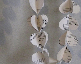 Pode incluir: Uma guirlanda de corações de papel branco com notas musicais pretas impressas neles. Os corações são enfiados juntos com fio branco.