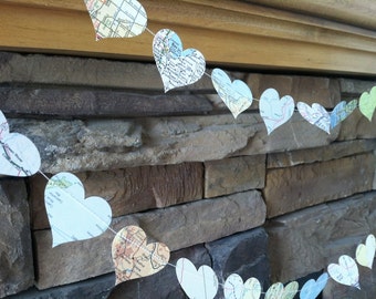 May include: A string of paper hearts decorated with maps, hanging against a stone wall. The hearts are connected with string and are in various shades of blue and green.
