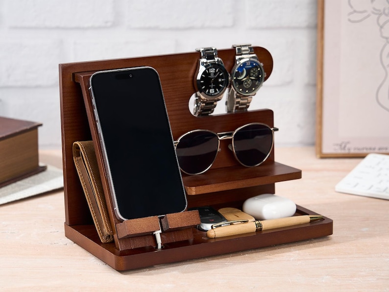 May include: A dark brown wooden desk organizer with compartments for a phone, wallet, sunglasses, watches, pen, keys, and earbuds. The organizer has a modern design and is made of wood.