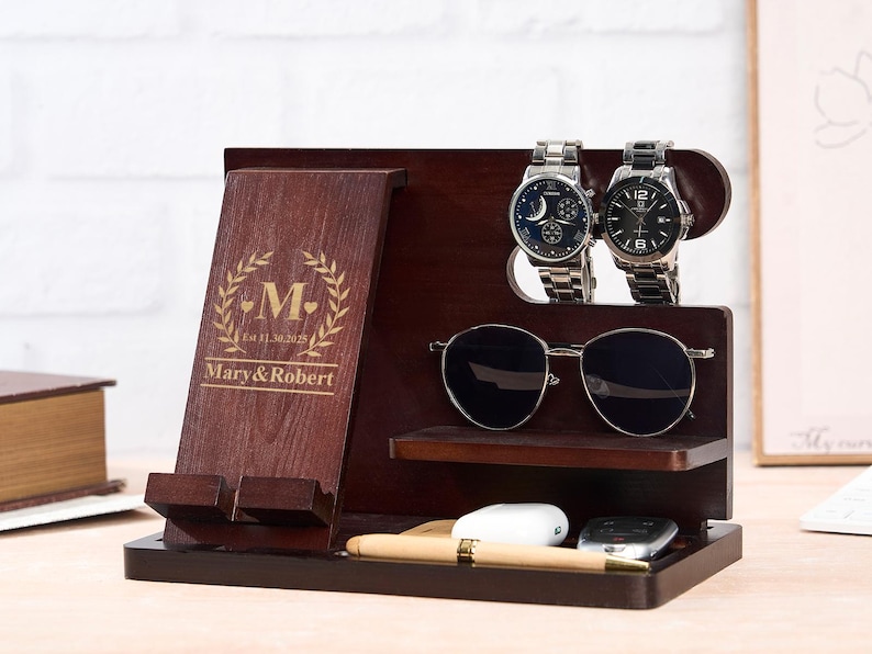 May include: A dark brown wooden organizer with a phone holder, watch holders, and a shelf for sunglasses. The organizer has the names "Mary & Robert" and the letter "M" with a laurel wreath design.