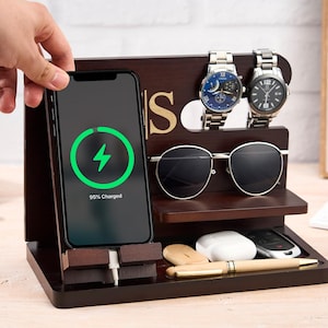 May include: A dark brown wooden charging station with a phone displaying a charging symbol. The station holds two watches, sunglasses, a pen, and other small items. The phone shows 95% charged.