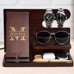 May include: A dark brown wooden organizer with a phone holder, two watches, sunglasses, and a small tray. The organizer is engraved with the name "Martin". The watches have silver bands and black faces. The sunglasses have black lenses.