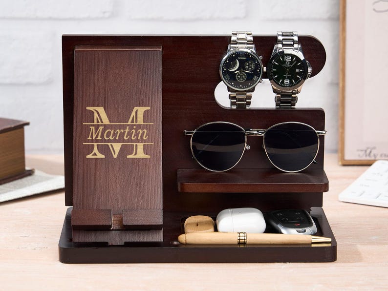 May include: A dark brown wooden organizer with a phone holder, two watches, sunglasses, and a small tray. The organizer is engraved with the name "Martin". The watches have silver bands and black faces. The sunglasses have black lenses.