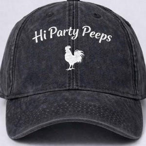 May include: A black baseball cap with the text "Hi Party Peeps" in white script above a white rooster graphic. The cap has a curved brim and a fabric strap closure.