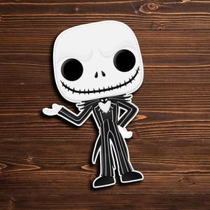 May include: A black and white Jack Skellington character from the Nightmare Before Christmas movie. The character is wearing a black and white striped suit with a black bow tie. The character is standing on a brown wooden surface.