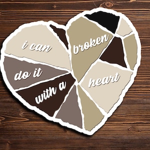 May include: A white heart-shaped sticker with a broken heart design. The heart is divided into multiple pieces with different shades of brown and beige. The text "I can do it with a broken heart" is written on the sticker.