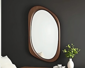 May include: An oval mirror with a brown wood frame and a bevelled edge. The mirror is hanging on a dark grey wall above a wooden dresser.