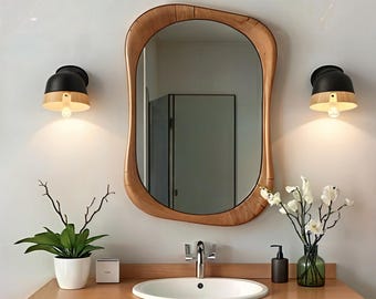 May include: A bathroom vanity with a white porcelain sink, a chrome faucet, and a wooden countertop. There is a wooden framed mirror with an irregular shape, two black and wood wall sconces, and a potted plant on the countertop.