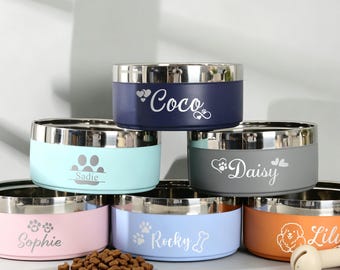 May include: A stack of six colorful stainless steel pet bowls with metallic rims. Each bowl is personalized with a name and graphic, including Coco, Sadie, Daisy, Sophie, Rocky, and Lily. A small pile of brown kibble and a beige bone toy are present.