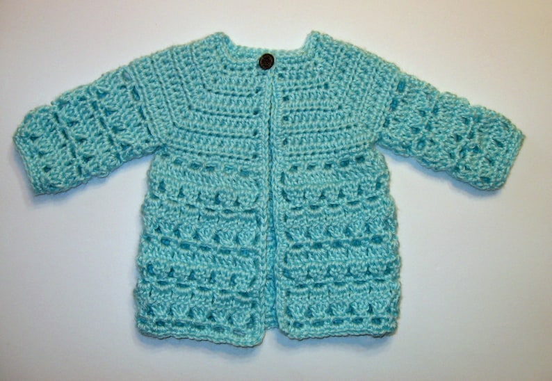 May include: A light blue crocheted cardigan with a button closure. The cardigan has a delicate stitch pattern and is perfect for a baby or toddler.