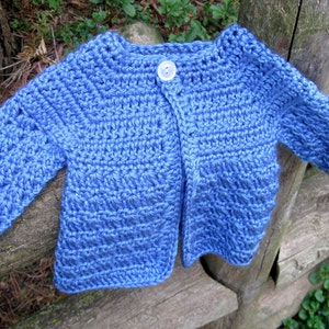 May include: A blue crocheted baby cardigan with a single button closure.