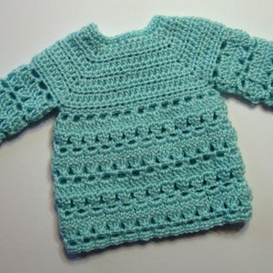 May include: A light blue crocheted baby sweater with a delicate open stitch pattern.
