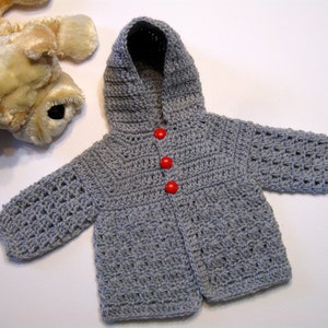 May include: A gray crocheted hooded jacket with red buttons. The jacket is made with a simple stitch pattern and has a classic design.