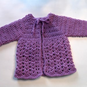 May include: A purple crocheted cardigan with a button closure and a tie at the neck.