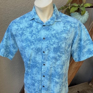 May include: A light blue short-sleeved button-down shirt with a white and blue tie-dye pattern.