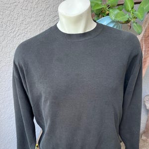 May include: A solid black long-sleeve crewneck sweatshirt featuring a ribbed collar, ribbed cuffs, and a ribbed hem. The garment is displayed on a mannequin torso, showcasing a plain, unpatterned design with a standard fit and a classic pullover style.