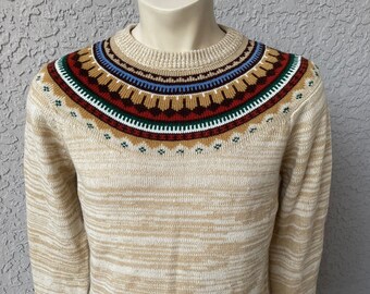 May include: A beige sweater with a colorful geometric pattern around the neckline. The sweater has a subtle marled effect.