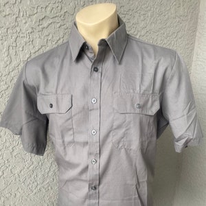 May include: A gray short-sleeved button-down shirt with two flap pockets on the chest.