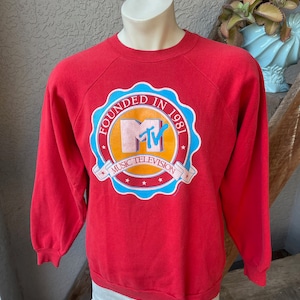 Puede incluir: Sudadera vintage roja con un logotipo circular que presenta el logotipo de MTV, el texto "Founded in 1981" y las palabras "Music Television".