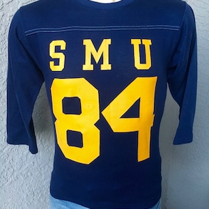 May include: A navy blue long-sleeved t-shirt with a yellow "SMU 84" graphic.