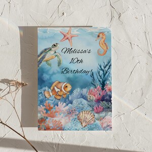 May include: A blue and green watercolor illustration of a sea turtle, a starfish, a seahorse, and a clownfish swimming in a coral reef. The text "Melissa's 10th Birthday!" is written in black cursive font.