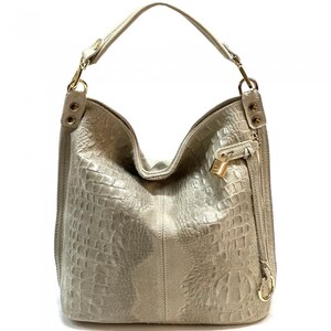 May include: A light beige leather handbag with a crocodile embossed pattern. The bag has a top zipper closure and a gold-toned lock detail. The bag has a long strap that can be worn on the shoulder or crossbody.