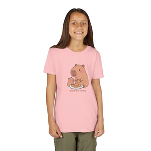 Puede incluir: Camiseta rosa claro con un dibujo animado de carpinchos compartiendo galletas. El texto "sharing is caring" está debajo. La camiseta la lleva una persona.