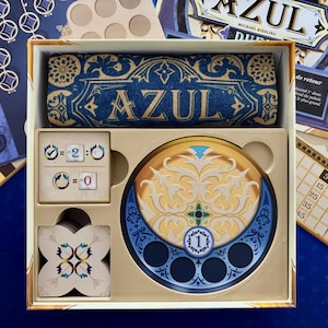 Peut inclure: Un gros plan sur les composants du jeu de société Azul, y compris le plateau de jeu, les tuiles et les jetons de score. Le plateau de jeu est de couleur brun clair avec un motif bleu et or. Les tuiles sont blanches avec des motifs bleus et or. Les jetons de score sont bleus et or.