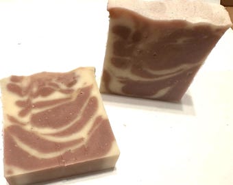 May include: Two bars of handmade soap with a creamy white and mauve swirl design. The soap has a rectangular shape with a smooth surface. The colors blend together, creating a marbled effect. The soap is likely scented and suitable for personal care.