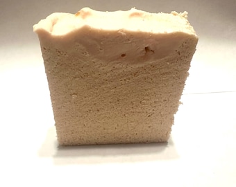 May include: A rectangular bar of handmade soap with a light beige body and a pale pink top layer. The soap has a textured appearance, suggesting a natural, artisanal quality. The top layer has a slightly uneven surface.