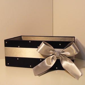May include: A dark blue velvet gift box with a silver satin bow and a rhinestone embellishment. The box is decorated with silver rhinestones.