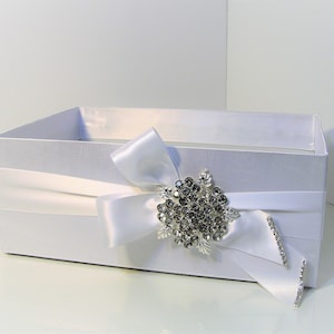 May include: White satin gift box with a white satin ribbon and a silver rhinestone brooch. The box is perfect for a wedding or other special occasion.