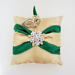 May include: A gold satin pillow with a green satin bow and a rhinestone brooch. The pillow is decorated with rhinestones and a gold and rhinestone mask.