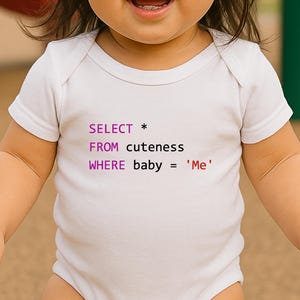 May include: White baby onesie with the text "SELECT * FROM cuteness WHERE baby = 'Me'" in purple and red. The onesie is short-sleeved and has a snap closure. The baby is smiling.