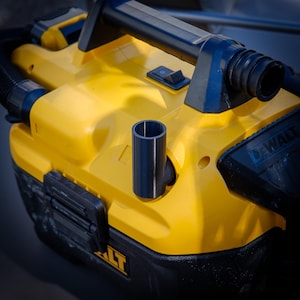 Pode incluir: Um aspirador portátil DeWalt amarelo e preto com uma pega preta e um bocal azul escuro. O aspirador tem um interruptor preto e um acessório azul escuro. O logótipo DeWalt é visível na lateral.