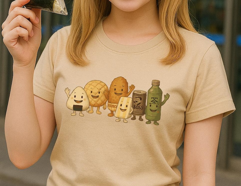 May include: A beige short-sleeved t-shirt featuring a graphic print of six anthropomorphic food and drink items, including an onigiri, a melon pan, a fried snack, a sandwich, a Boss coffee can, and a green tea bottle, all with smiling faces.