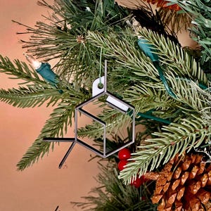 May include: A silver 3D printed Christmas ornament shaped like a molecule hanging on a green artificial Christmas tree.