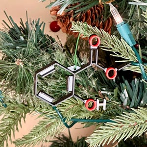 May include: A black and white 3D printed Christmas ornament shaped like a molecule with red oxygen atoms. The ornament is hanging on a green artificial Christmas tree.