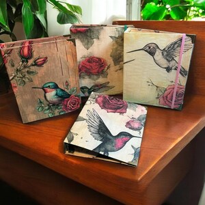 May include: Four decorative journals with floral and hummingbird designs. The journals have a rustic, vintage aesthetic and feature a variety of colors, including pink, green, blue, and brown.