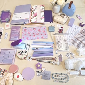 May include: A collection of stationery and accessories in shades of purple, white, and floral patterns, including lined notebooks, pens, a pencil case, stickers, a reading log, a small bag, a white headband, and various decorative paper clips and charms.