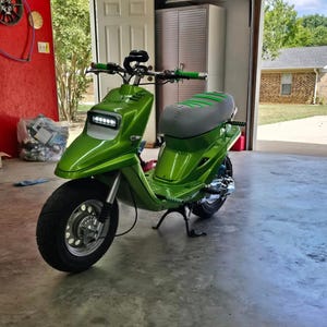 May include: A custom green scooter with a gray seat and green accents. The scooter has a large front tire, a headlight, and green handlebars. It is parked inside a garage.
