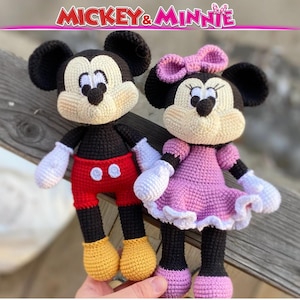 Puede incluir: Muñecos de Mickey y Minnie Mouse tejidos a crochet. Mickey lleva pantalones cortos rojos, zapatos amarillos y orejas negras. Minnie lleva un vestido rosa, un lazo rosa y orejas negras. El texto "Mickey & Minnie" está arriba.