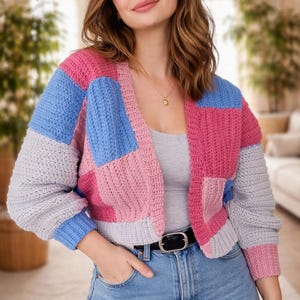 Peut inclure: Un cardigan en crochet patchwork aux tons rose, bleu et gris. Le pull ouvert présente un col en V et des manches longues. Le modèle porte un jean bleu et une ceinture noire.