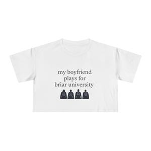 Puede incluir: Una camiseta corta blanca con el texto negro 'my boyfriend plays for briar university' centrado en el pecho. Debajo del texto hay cuatro siluetas de camisetas oscuras con los números 46, 22, 44 y 66 impresos en color blanco.