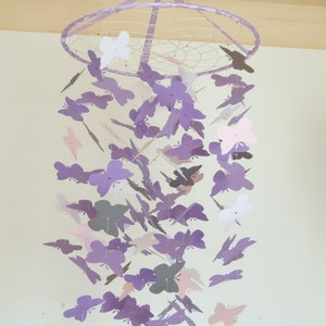 May include: A purple, pink, and white butterfly mobile hanging from a white ceiling. The mobile is made of paper butterflies and has a wire frame.