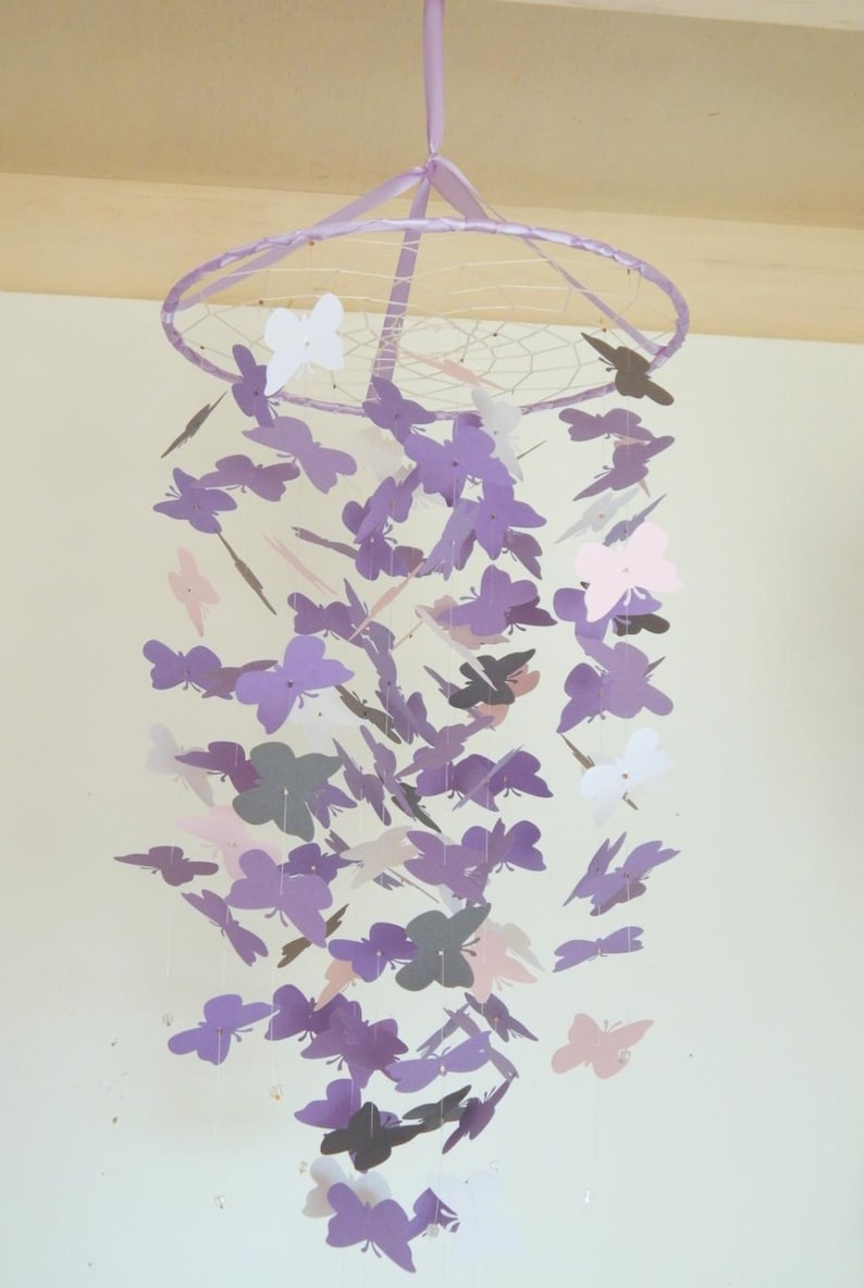 May include: A purple, pink, and white butterfly mobile hanging from a white ceiling. The mobile is made of paper butterflies and has a wire frame.