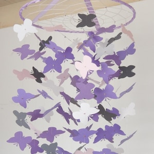 May include: A purple and gray butterfly mobile with a circular hoop and multiple butterflies hanging from it. The butterflies are made of paper and are in various shades of purple, gray, and white.