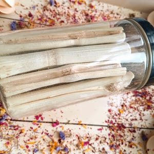 Pu&ograve; includere: Un barattolo di vetro trasparente con coperchio nero pieno di bastoncini di bamb&ugrave; colorati. Il barattolo &egrave; appoggiato su una superficie di legno bianco cosparsa di petali di fiori secchi e piccoli cucchiai di legno. I bastoncini di bamb&ugrave; sono cilindrici.