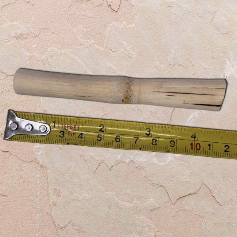 Pu&ograve; includere: Un bastoncino di bamb&ugrave; di colore chiaro, lungo circa 25 cm, &egrave; adagiato accanto a un metro a nastro giallo. Il metro a nastro mostra le misure in pollici e piedi. Il bastoncino di bamb&ugrave; ha un aspetto naturale e non verniciato.
