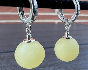 May include: A pair of silver hoop earrings with a dangling yellow orb charm. The orbs are frosted and have a matte finish.